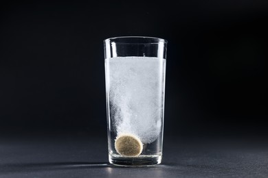 Effervescent pill dissolving in glass of water on grey table