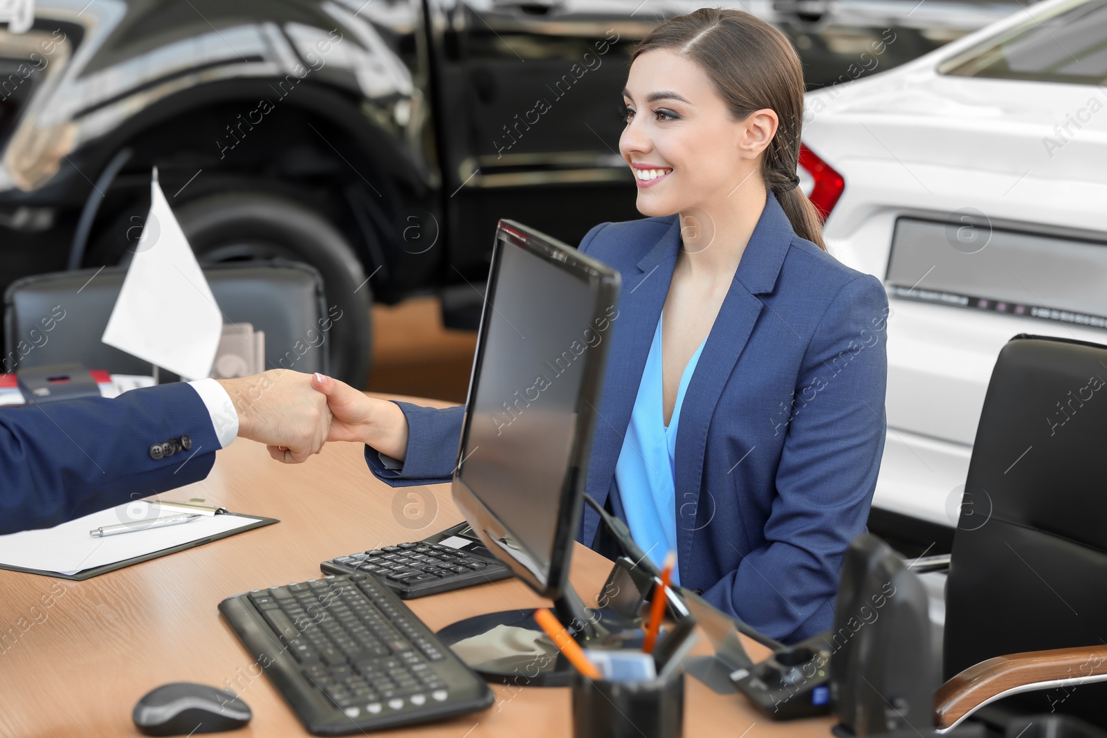 Photo of Young woman shaking hands with salesman in car salon