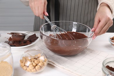 Woman mixing delicious chocolate cream with whisk at white wooden table indoors, closeup