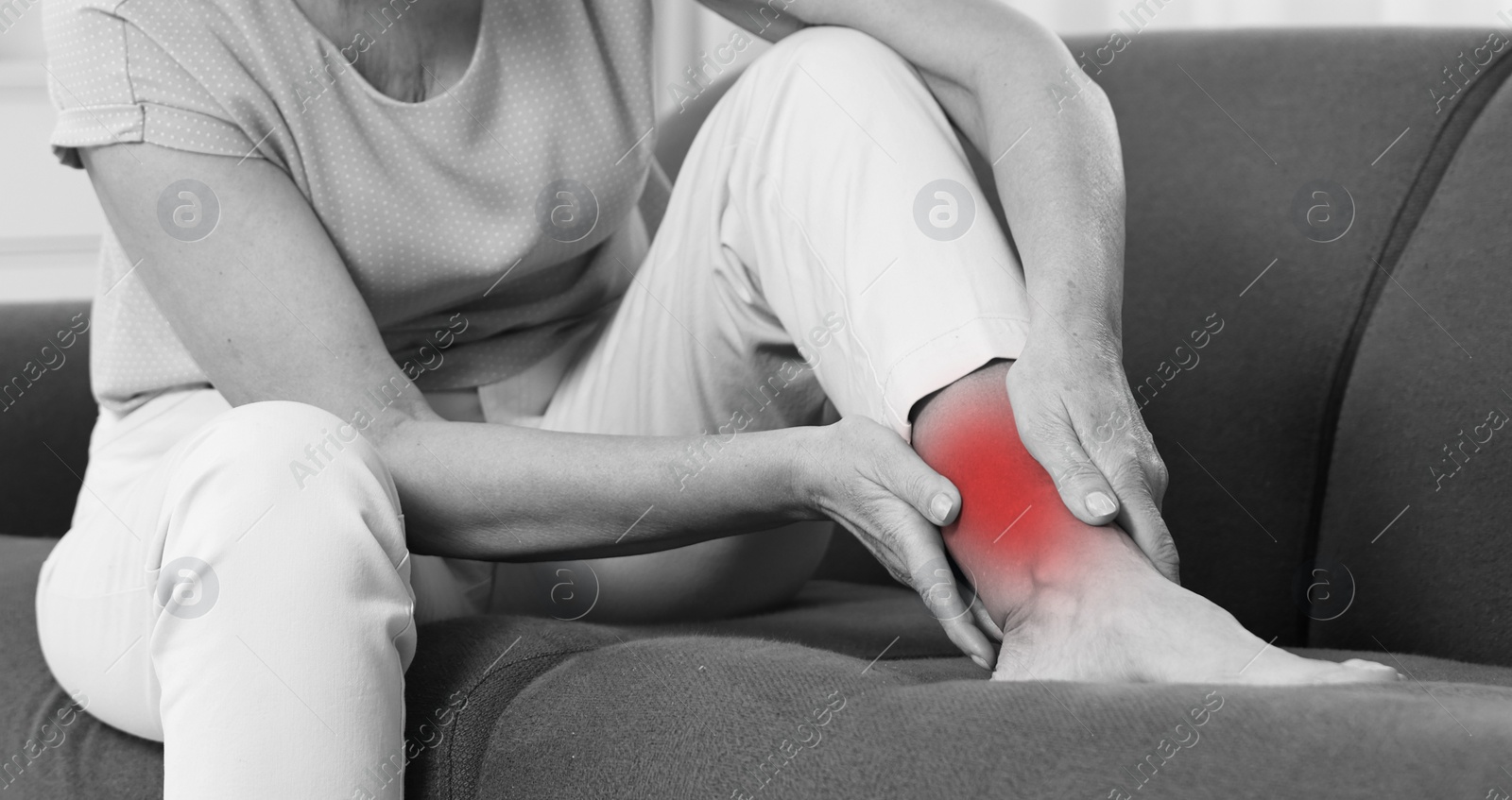 Image of Woman suffering from pain in ankle on sofa, closeup. Black and white effect. Banner design