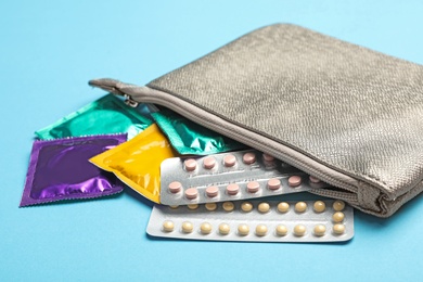 Photo of Cosmetic bag with condoms and birth control pills on light blue background. Safe sex concept