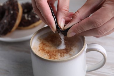 Woman adding sugar to tasty coffee at white wooden table, closeup