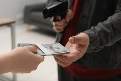 Photo of Woman giving money to criminal with gun indoors, closeup. Armed robbery