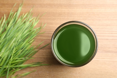 Glass of spirulina drink and wheatgrass on wooden table, top view with space for text