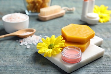 Photo of Lip balm, natural beeswax and flower on blue wooden table