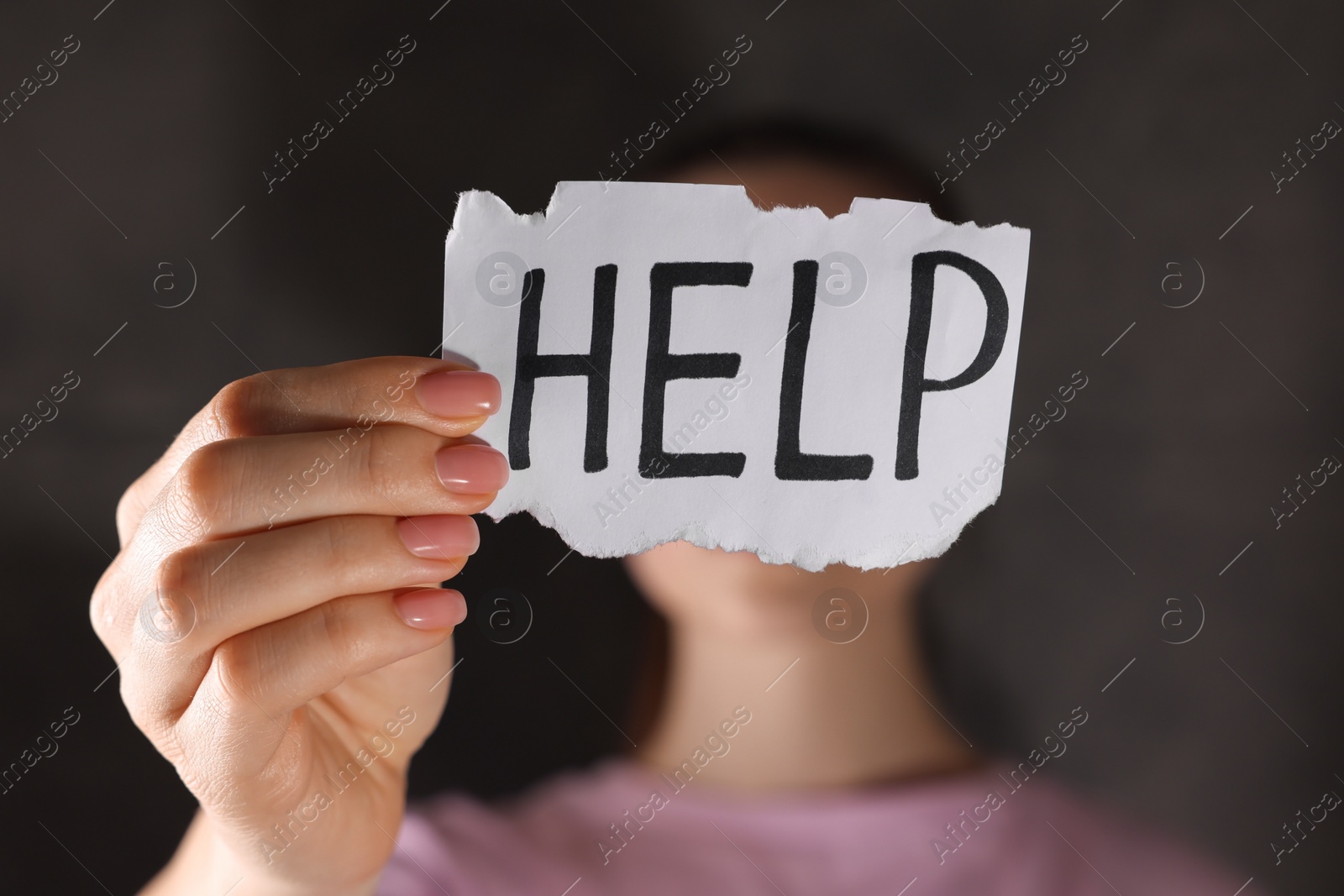 Photo of Woman holding piece of paper with word Help on dark background, closeup. Domestic violence concept