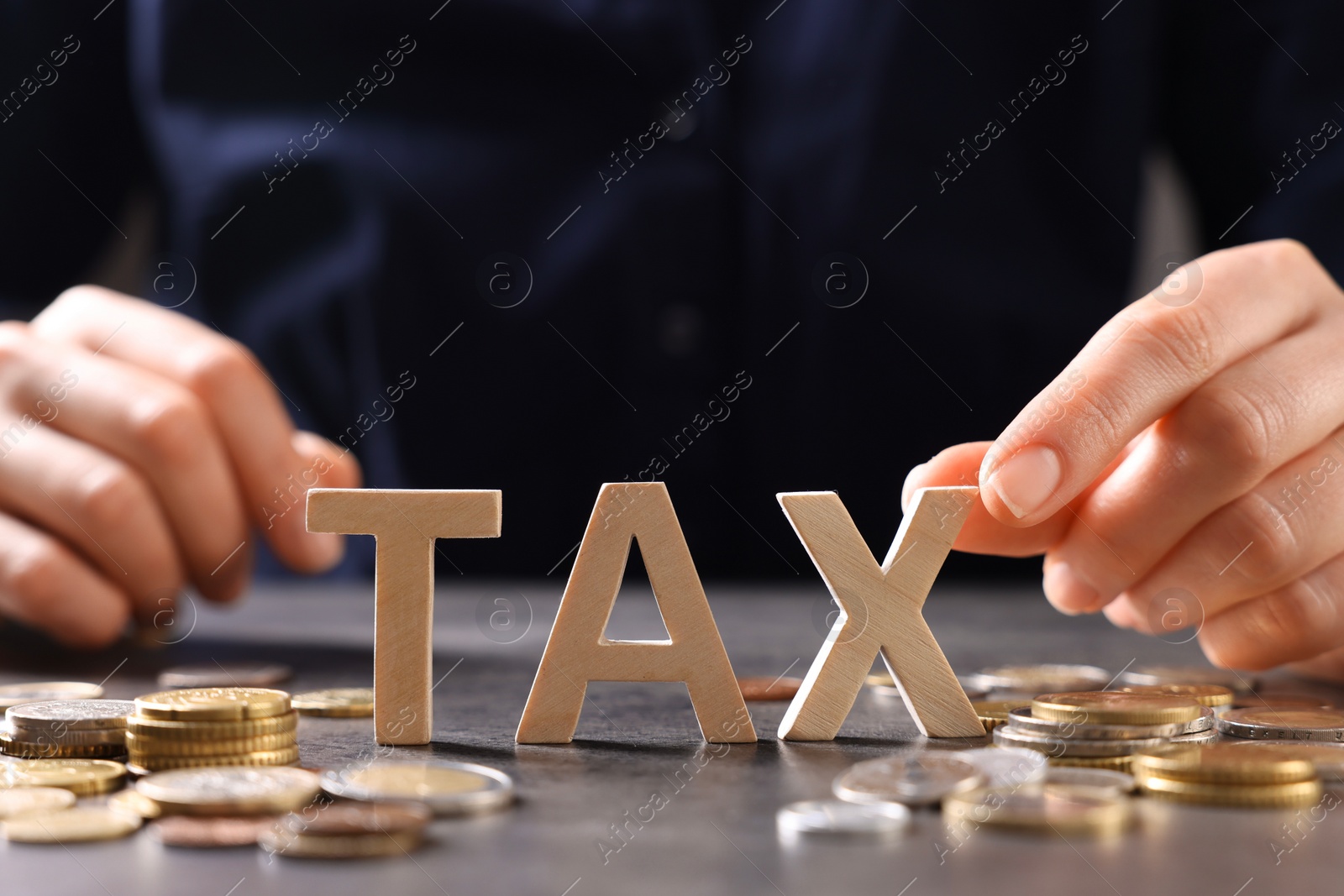 Photo of Woman with word Tax, wooden cubes and coins at grey table, closeup