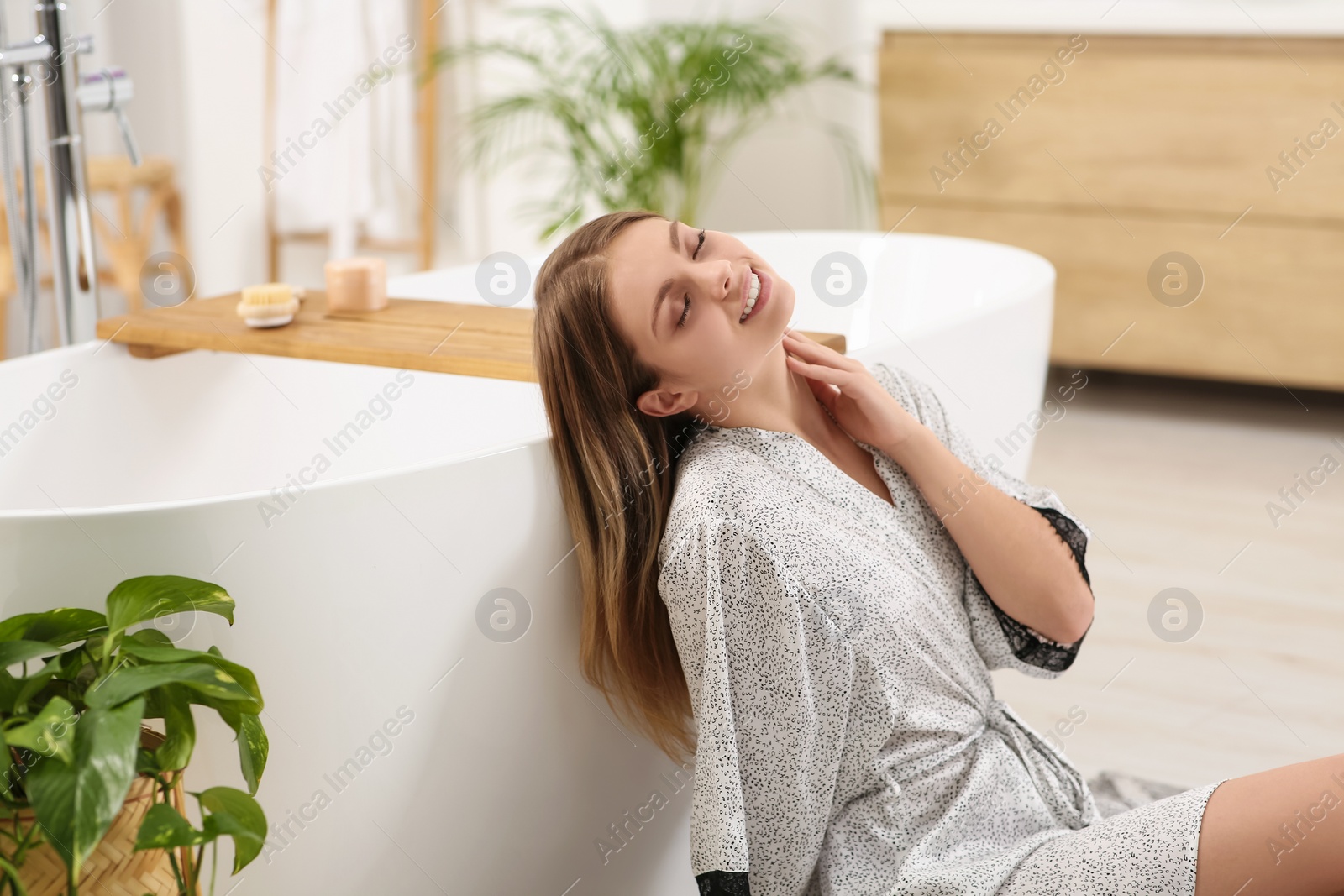 Photo of Beautiful happy woman in stylish robe near bath tub indoors