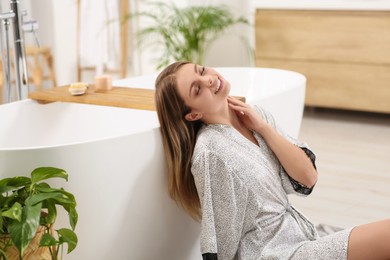 Beautiful happy woman in stylish robe near bath tub indoors