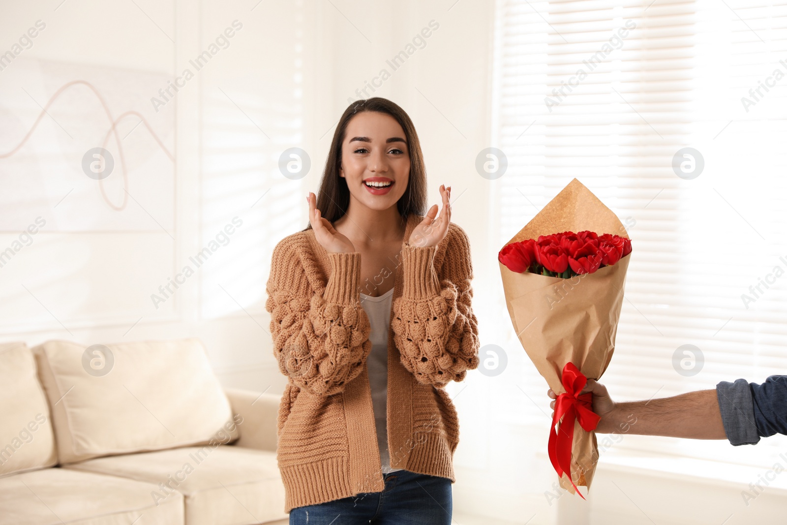 Photo of Happy woman receiving red tulip bouquet from man at home. 8th of March celebration