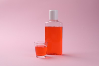 Photo of Fresh mouthwash in bottle and glass on pink background