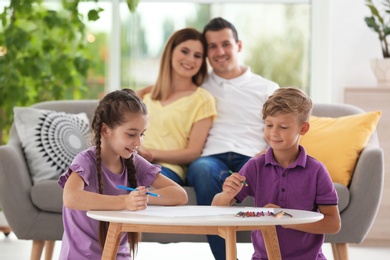 Photo of Children drawing at table near parents indoors. Happy family