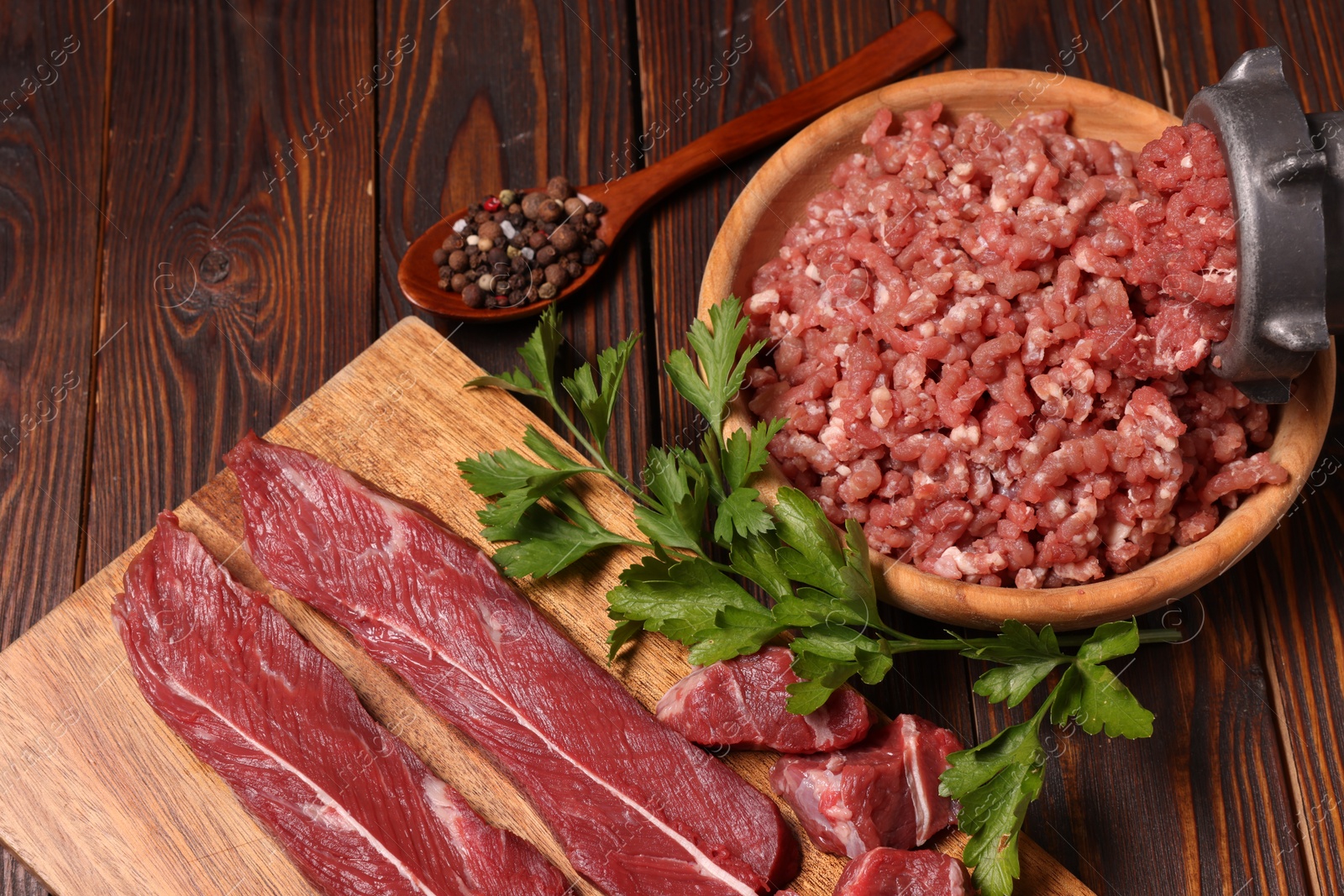 Photo of Manual meat grinder with beef, parsley and peppercorns on wooden table, above view