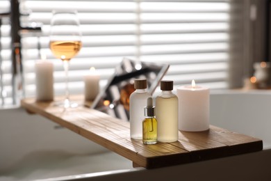 Photo of Wooden tray with tablet, wine, candles and toiletries on bathtub in bathroom, selective focus