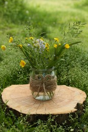 Photo of Bouquet of beautiful wildflowers in glass vase on wooden stump outdoors