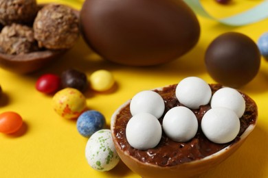 Photo of Tasty chocolate eggs and candies on yellow background, closeup