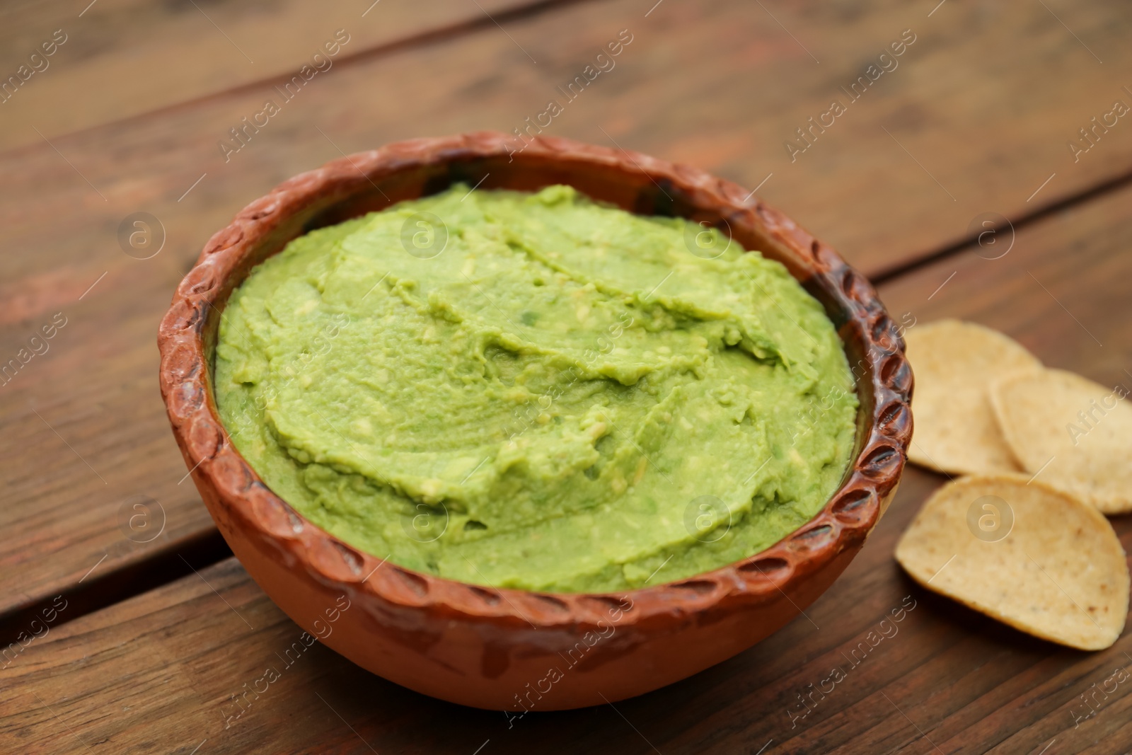 Photo of Delicious guacamole made of avocados and chips on wooden table, closeup