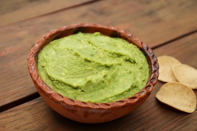 Delicious guacamole made of avocados and chips on wooden table, closeup