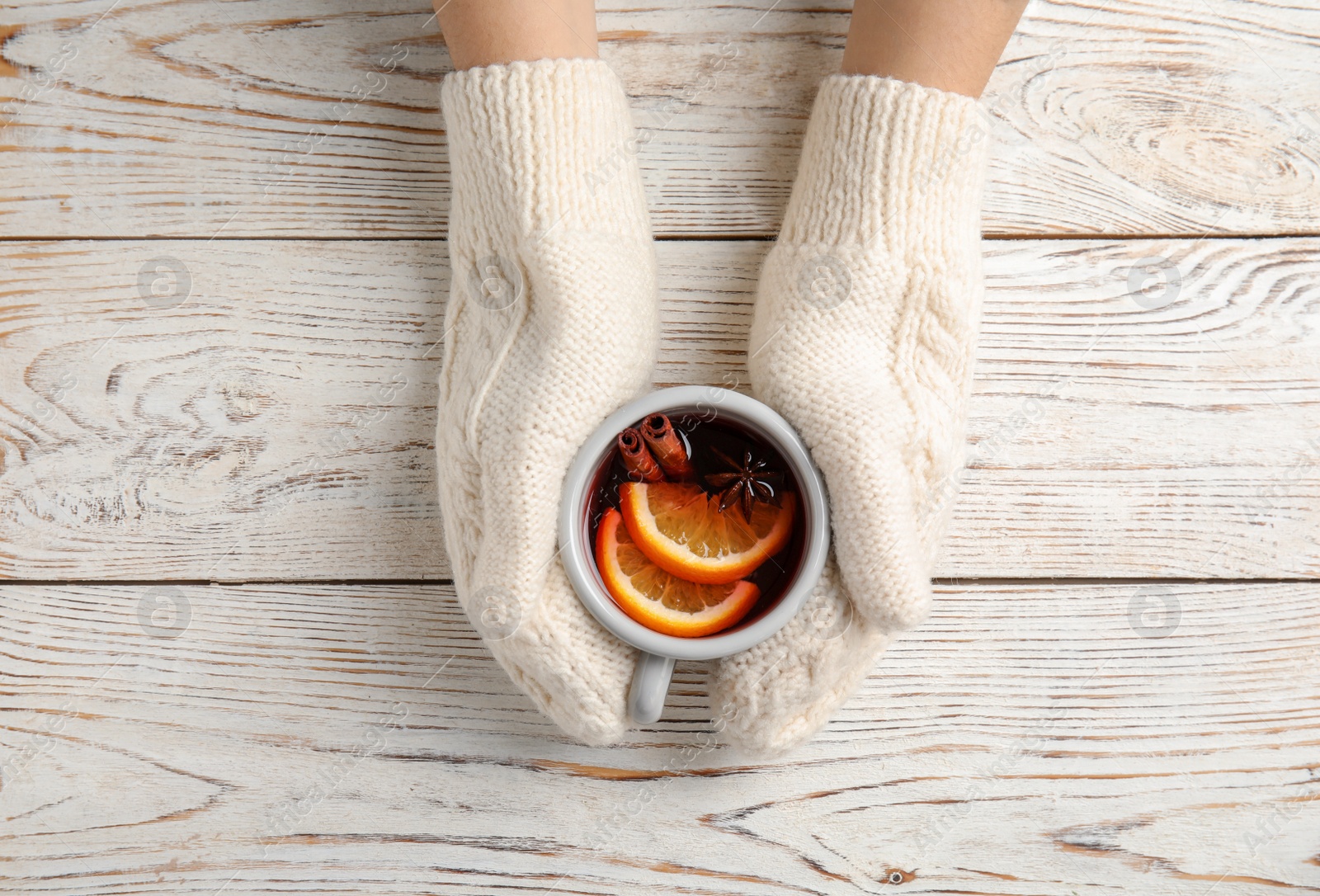 Photo of Woman with knitted mittens holding hot winter drink on wooden background, top view. Cozy season