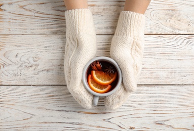 Woman with knitted mittens holding hot winter drink on wooden background, top view. Cozy season