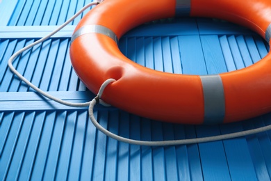 Photo of Orange lifebuoy on blue wooden background, closeup. Rescue equipment