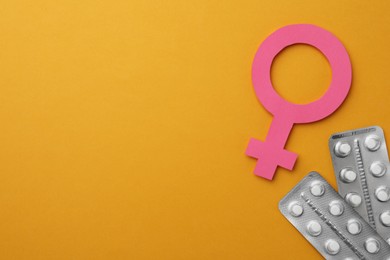 Photo of Female gender sign, blisters of pills and space for text on orange background, flat lay. Women's health concept
