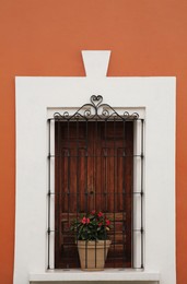 Photo of Orange building with wooden window and potted plant on windowsill outdoors