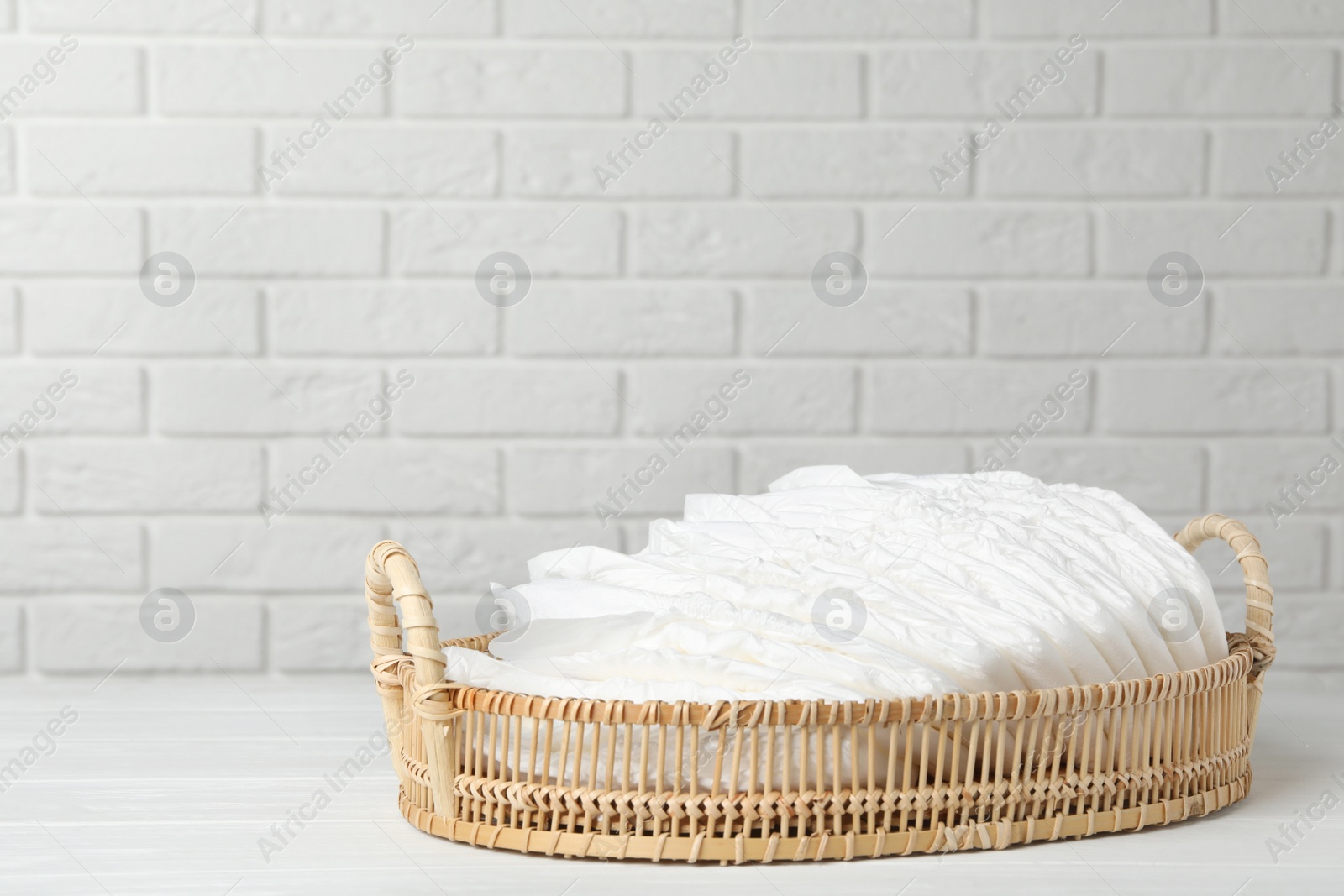 Photo of Tray with baby diapers on wooden table against white brick wall. Space for text