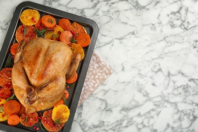 Roasted chicken with oranges, pomegranate and vegetables on white marble table, top view. Space for text