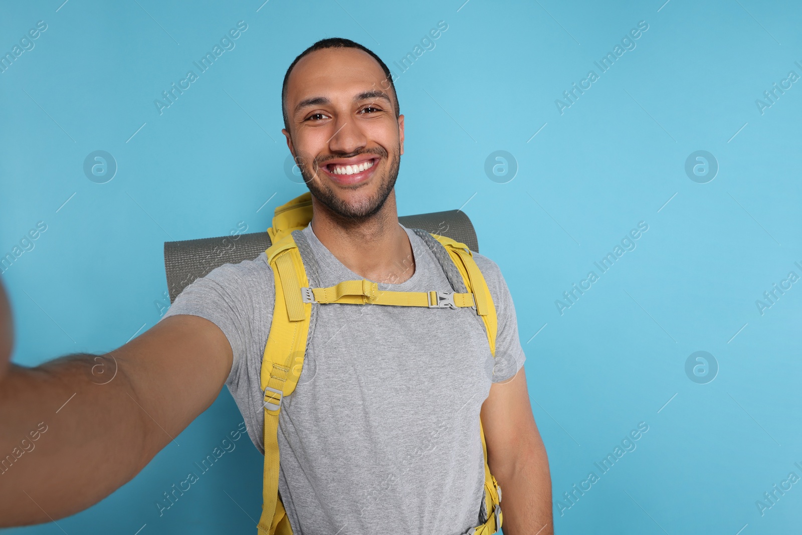 Photo of Happy tourist with backpack taking selfie on light blue background, space for text