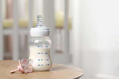 Feeding bottle with milk and pacifier on wooden table indoors. Space for text