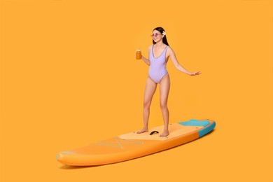 Photo of Happy woman with refreshing drink chilling on SUP board against orange background