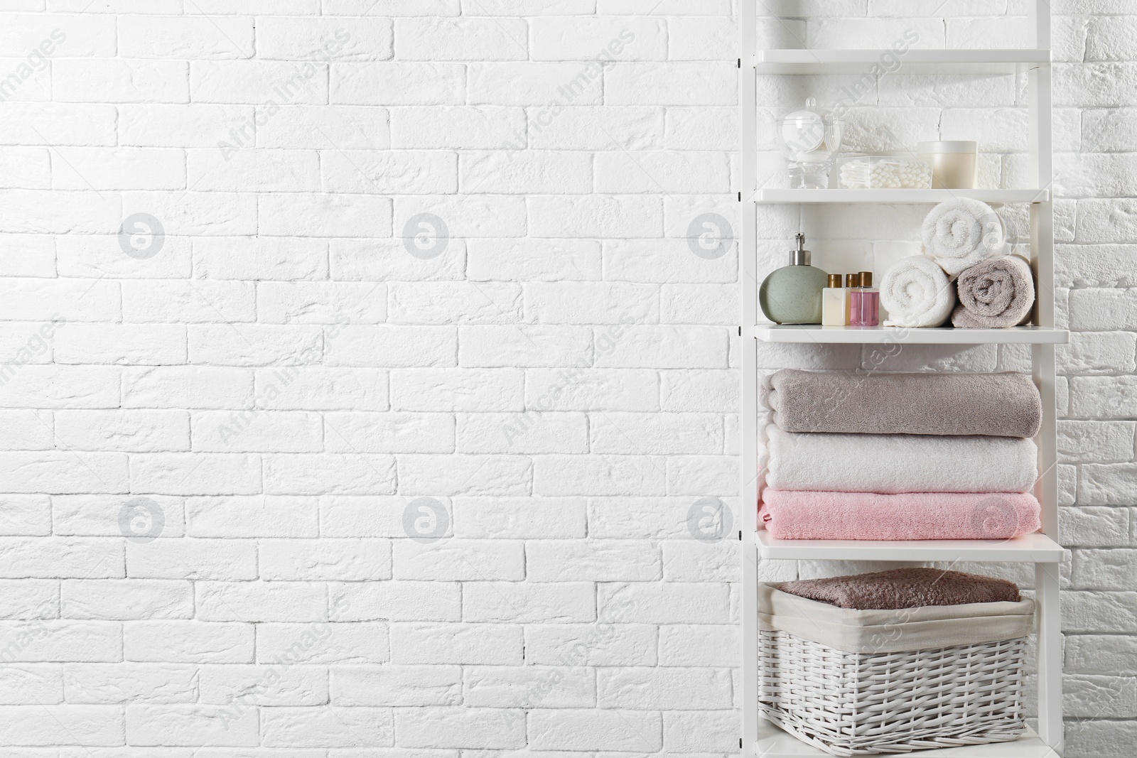 Photo of Shelving unit with clean towels and toiletries near brick wall. Space for text