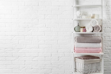 Shelving unit with clean towels and toiletries near brick wall. Space for text