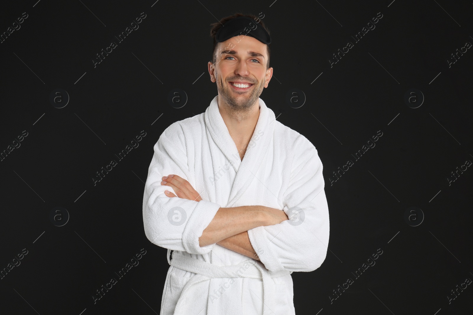 Photo of Happy young man in bathrobe and eye sleeping mask on black background