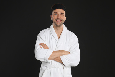 Happy young man in bathrobe and eye sleeping mask on black background