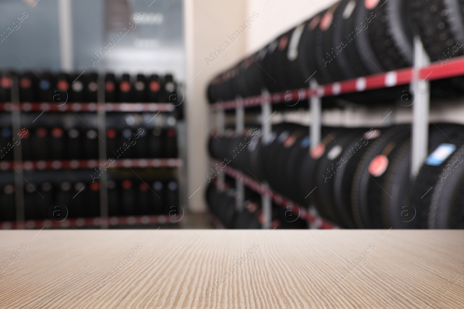 Image of Empty wooden surface and blurred view of car tires in auto store, closeup. Space for text 