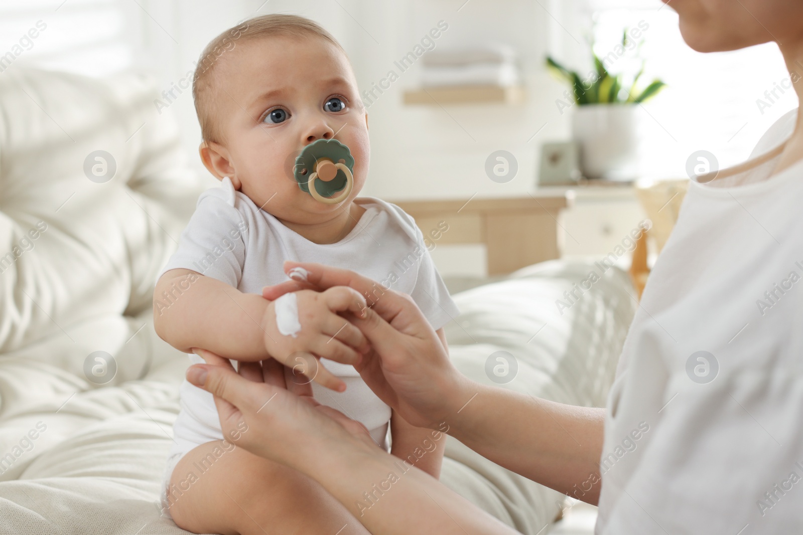 Photo of Mother applying body cream on her little baby at home, closeup