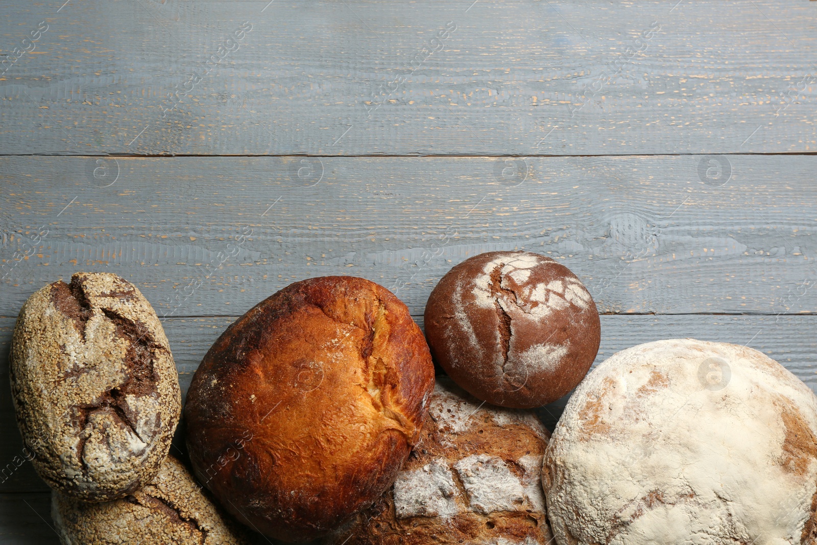 Photo of Different kinds of delicious bread on grey wooden table, flat lay. Space for text