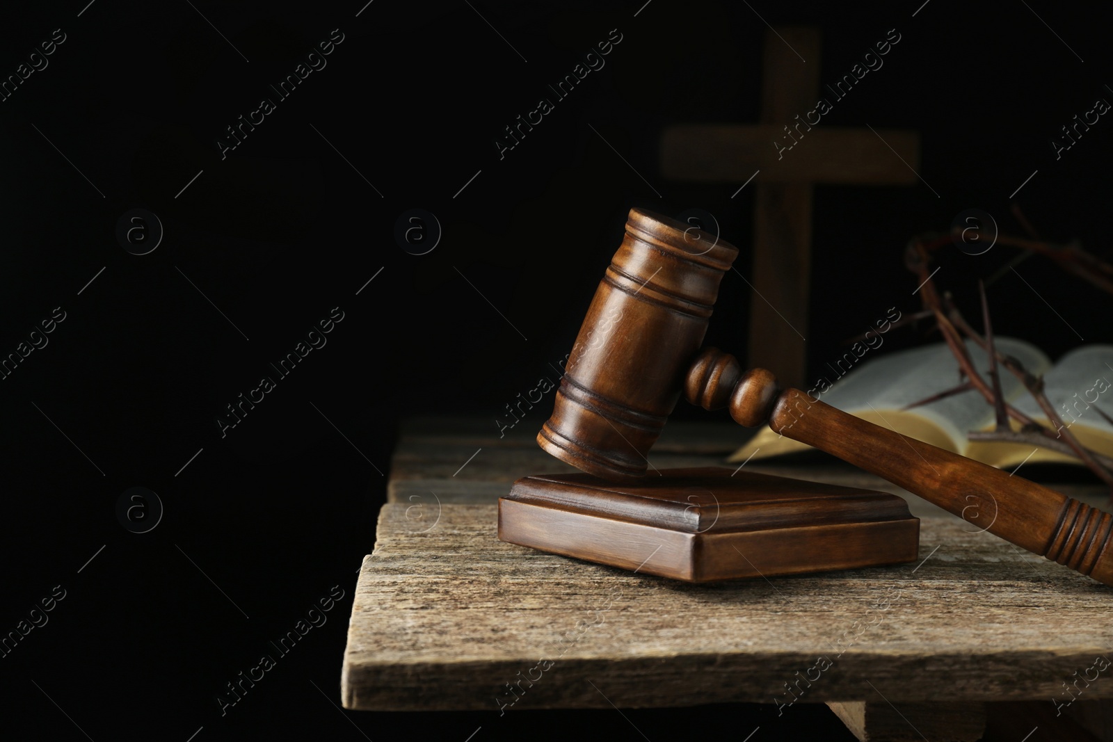 Photo of Judge gavel, bible, cross and crown of thorns on wooden table against black background. Space for text