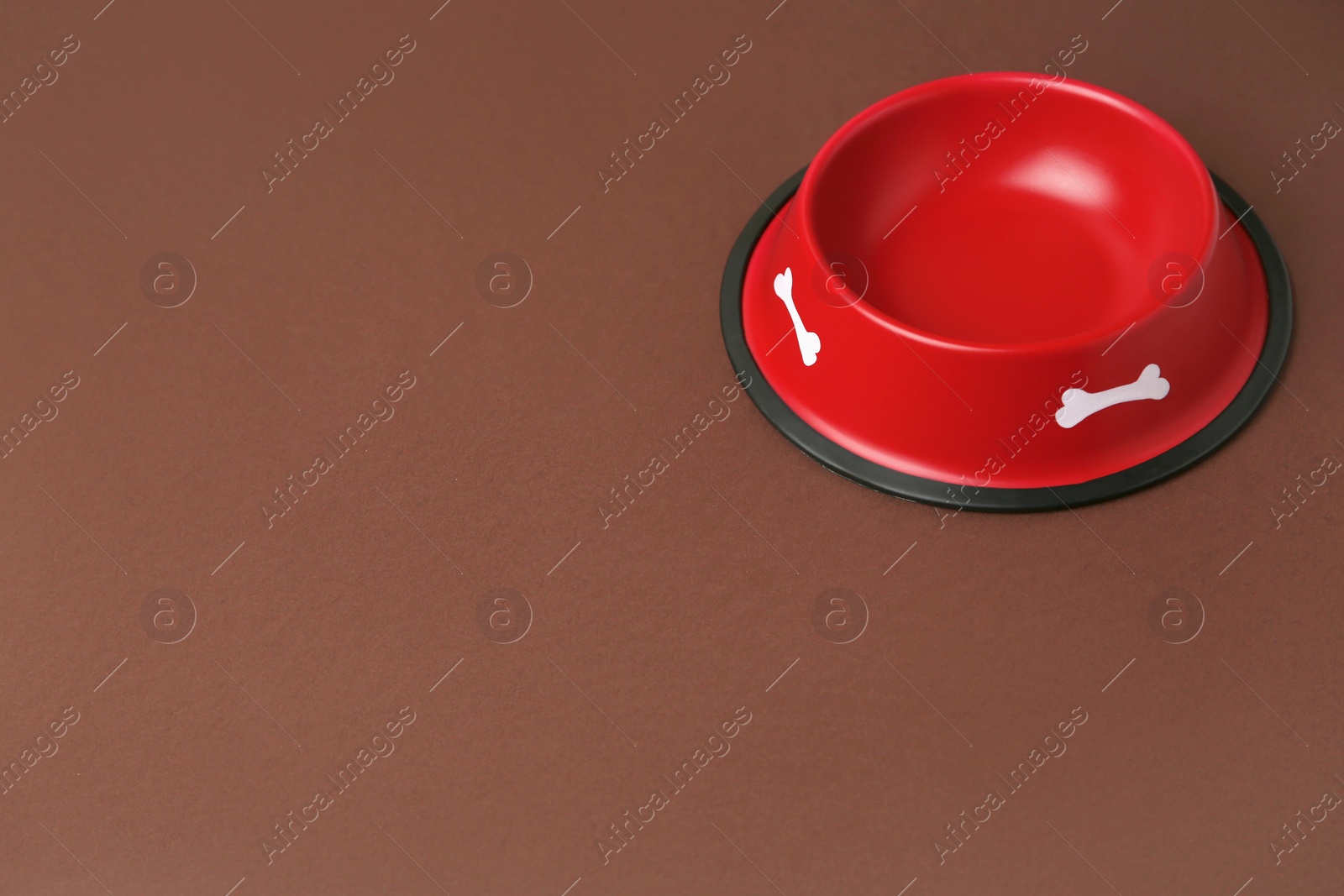 Photo of Empty red feeding bowl on brown background. Space for text