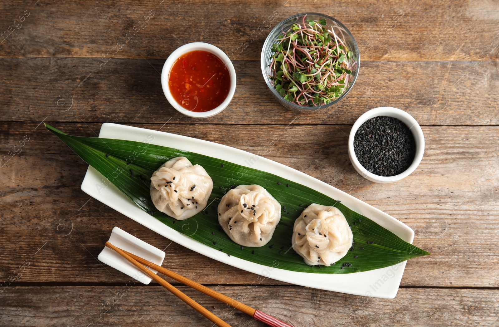 Photo of Flat lay composition with plate of tasty baozi dumplings, sesame seeds, sprouts and sauce on wooden table