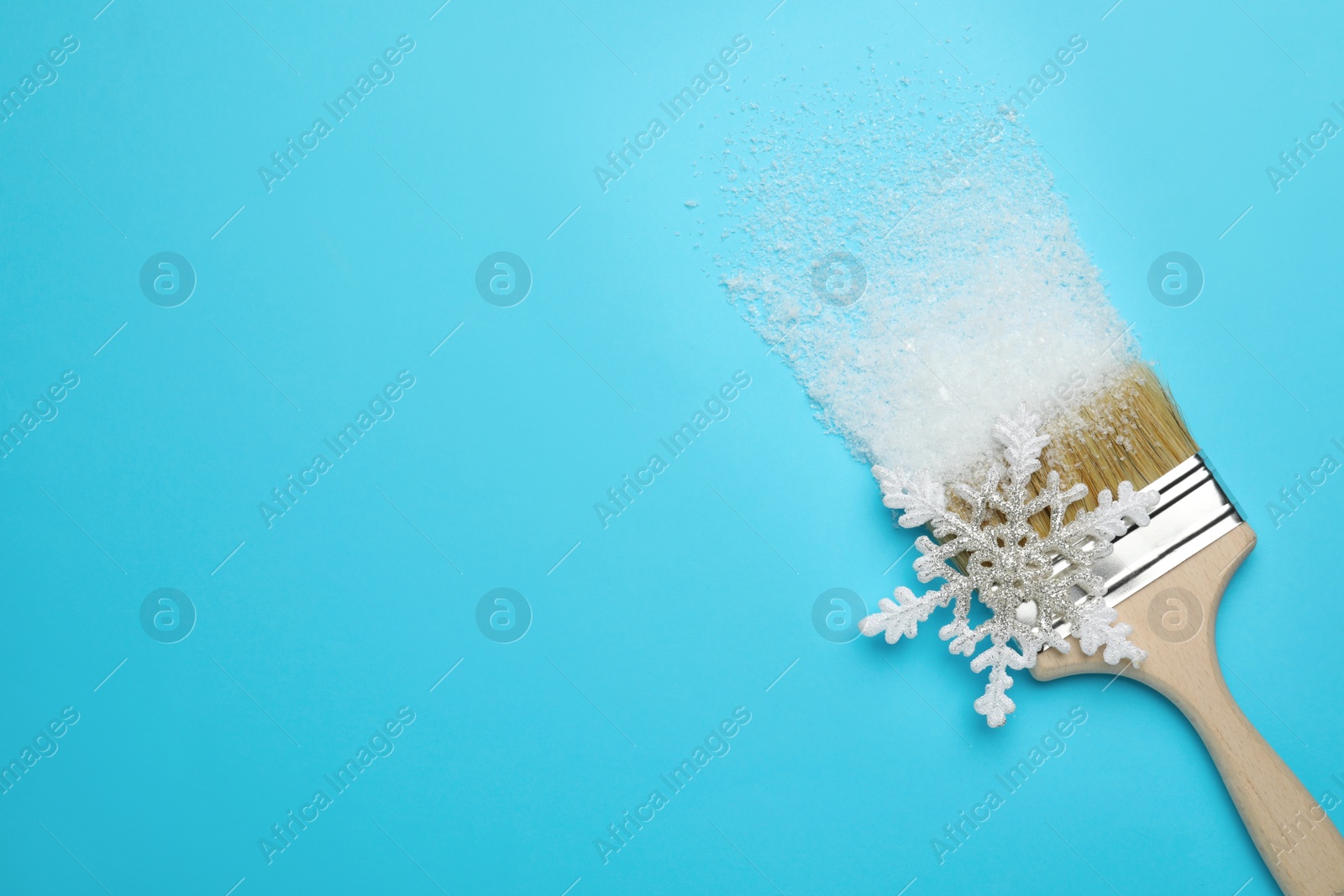 Photo of Brush painting with artificial snow on light blue background, top view. Space for text. Creative concept