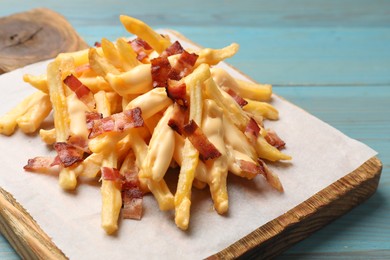 Photo of Delicious French fries with bacon and cheese sauce on light blue wooden table, closeup