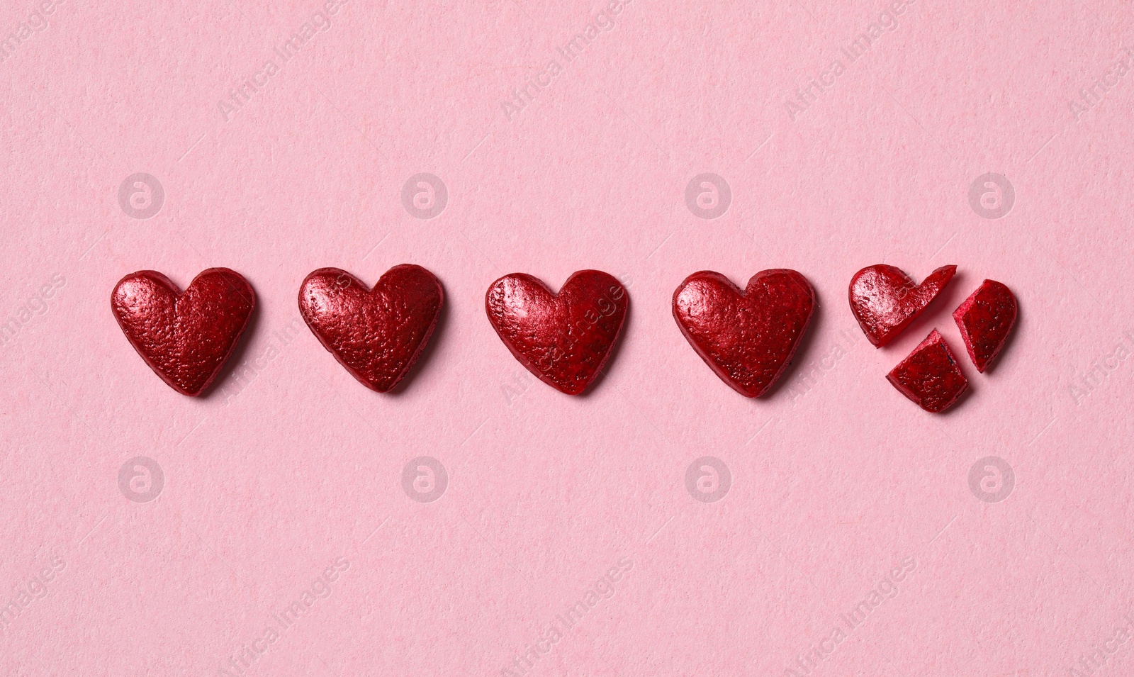 Photo of Red heart shaped sprinkles and one broken on pink background, flat lay