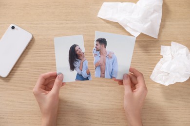 Woman holding torn photo near paper napkins at wooden table, top view. Divorce concept