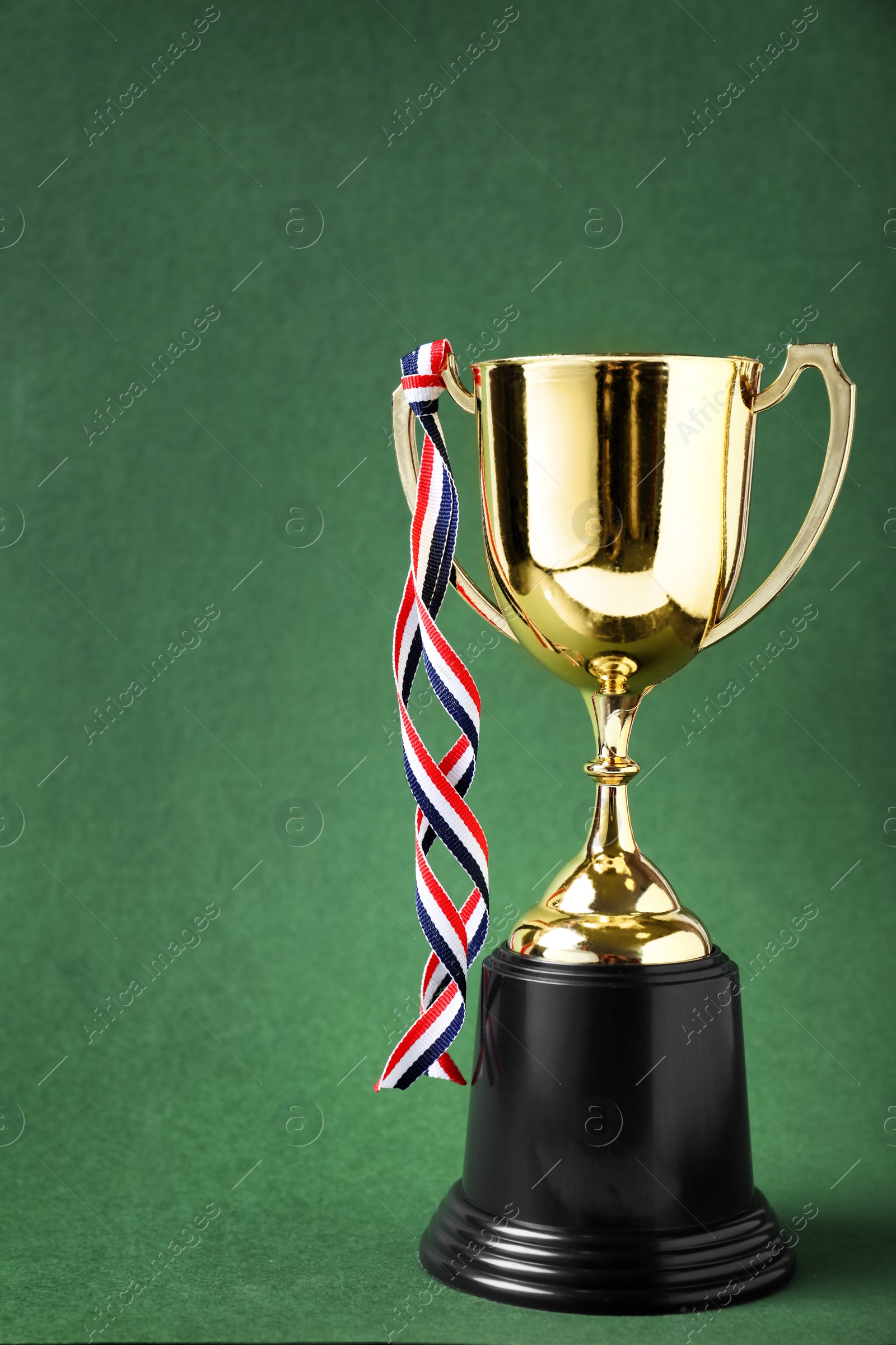 Photo of Golden trophy cup with ribbon on green background