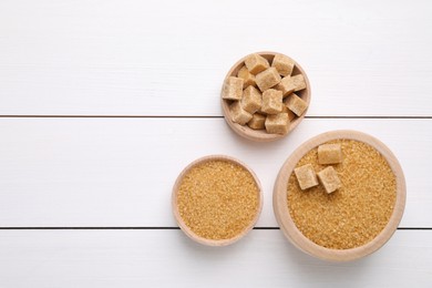 Photo of Different types of brown sugar in bowls on white wooden table, flat lay. Space for text