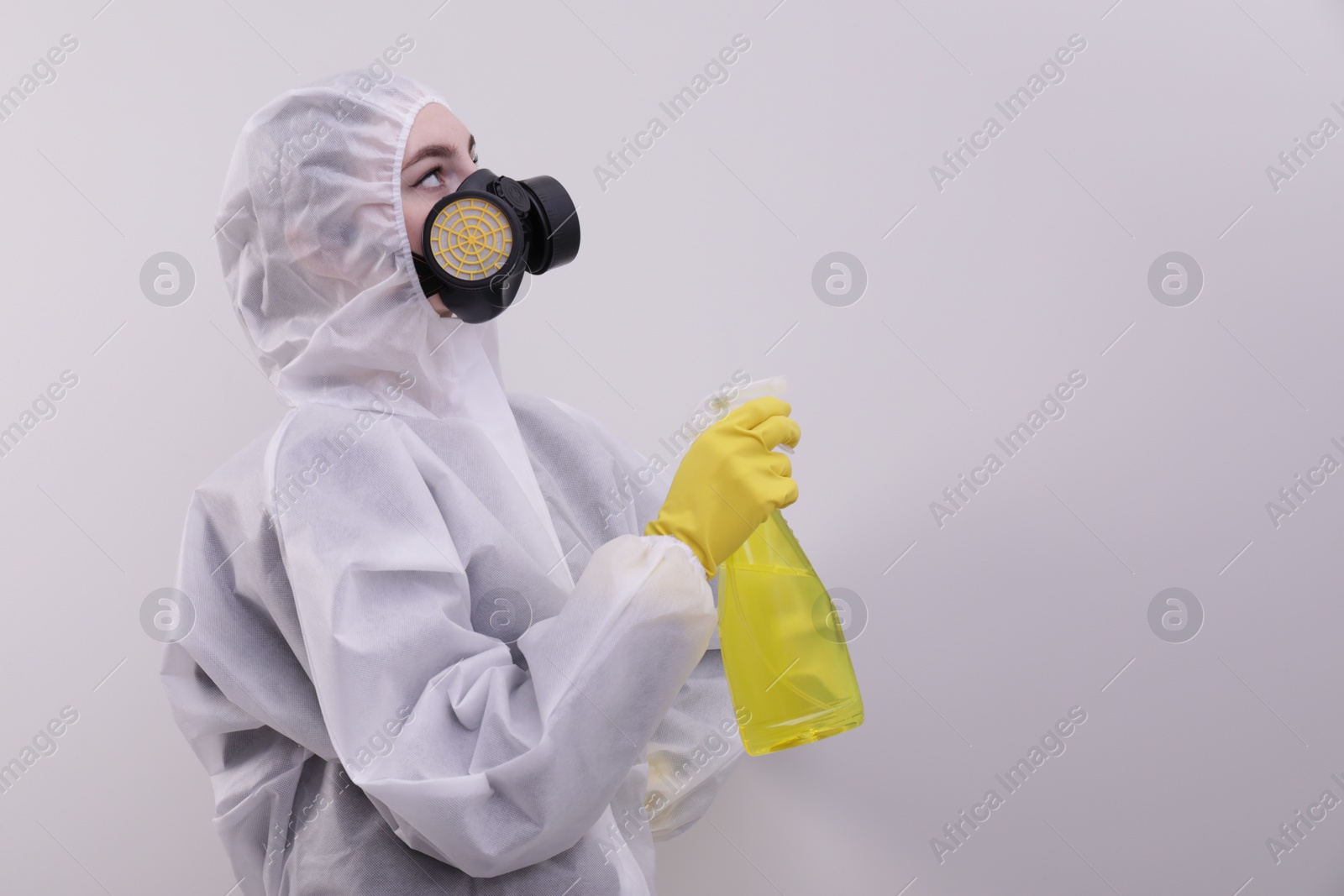 Photo of Woman in protective suit cleaning mold with sprayer on wall. Space for text