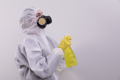 Woman in protective suit cleaning mold with sprayer on wall. Space for text